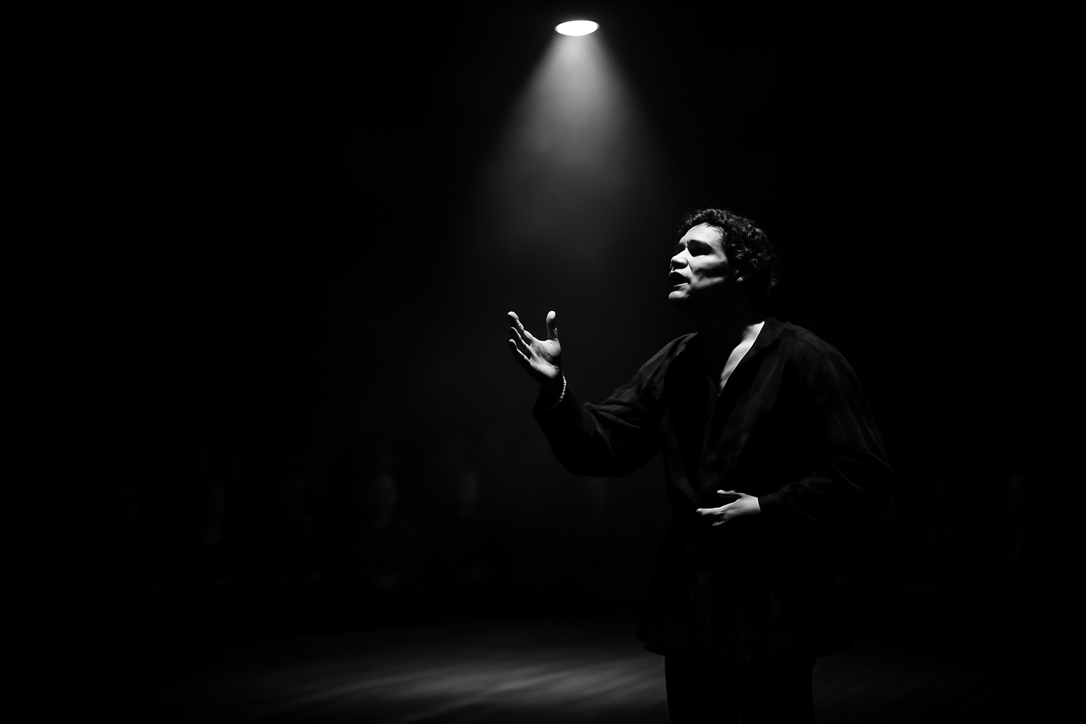 "Actor performing soliloquy under spotlight in dark theatre"