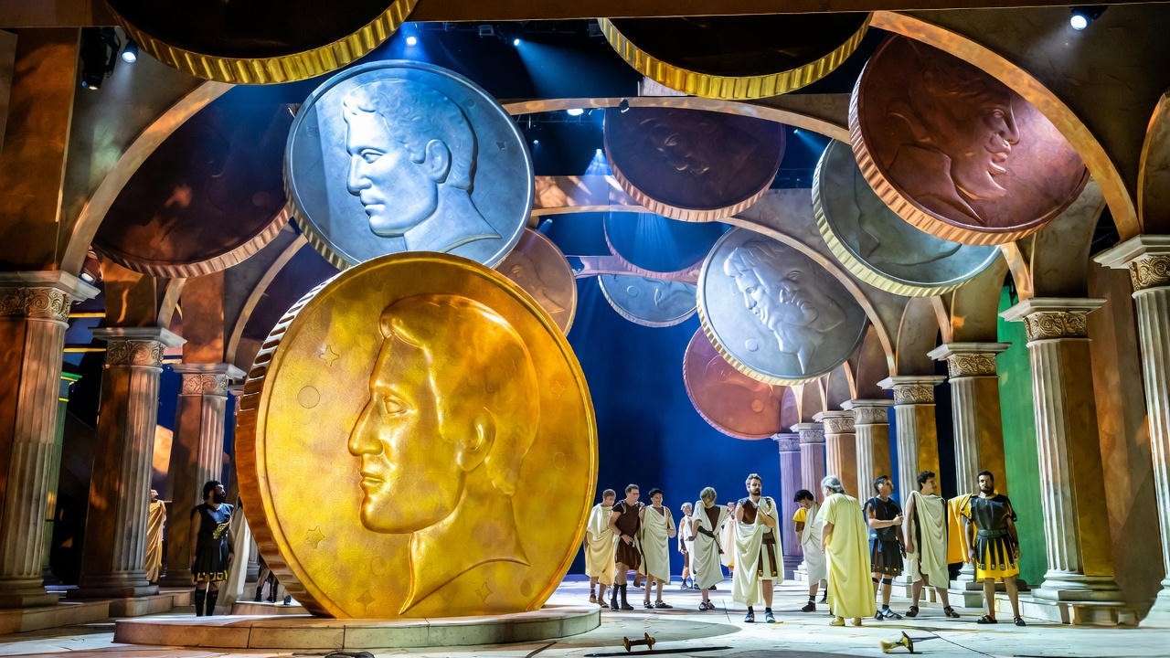 Modern Julius Caesar stage with oversized coin motifs and actors