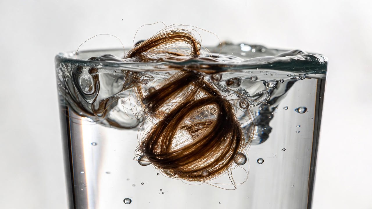 Hair porosity float test showing high-porosity strand sinking in water glass