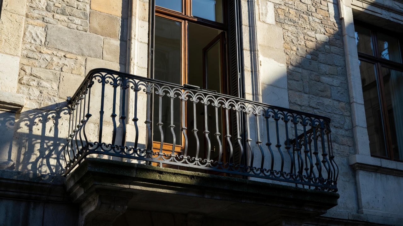 Traditional wrought-iron Juliette balcony with ornate railings on French doors, illustrating the shallow non-protruding design.