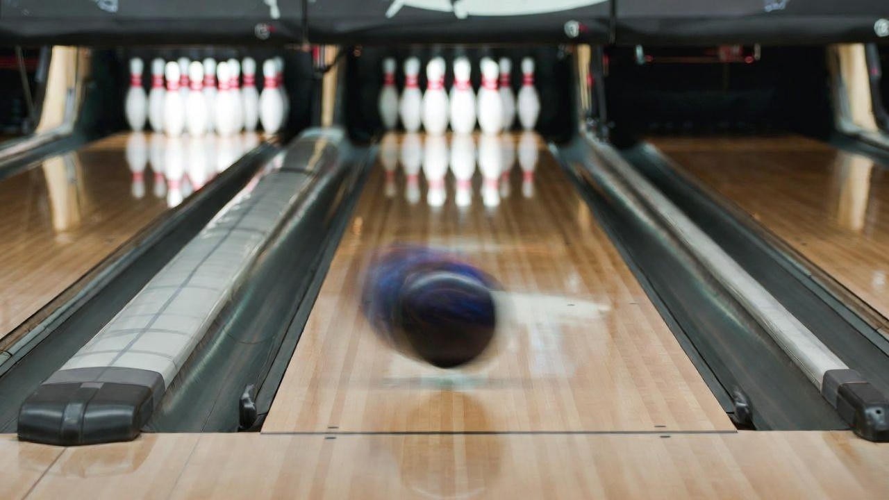 Bowling ball with strong hook motion on a heavy oil lane pattern, approaching the pins for a strike.