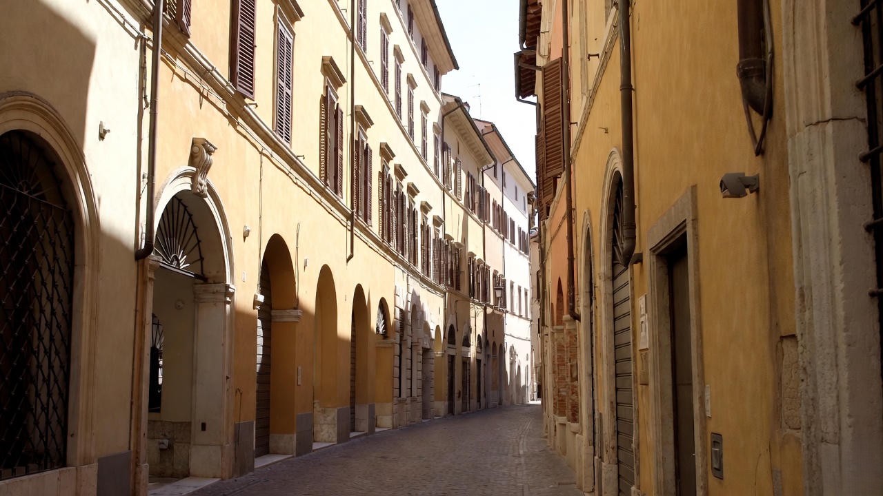 Narrow cobblestone street in Renaissance Verona under harsh summer sun, evoking the tense public spaces where feuds erupt in Romeo and Juliet