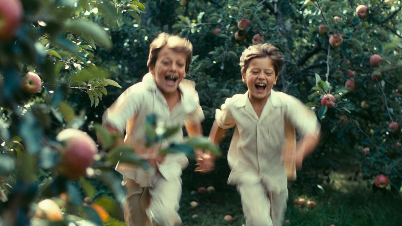 Playful cousins chasing each other in a summer orchard evoking nostalgic childhood memories