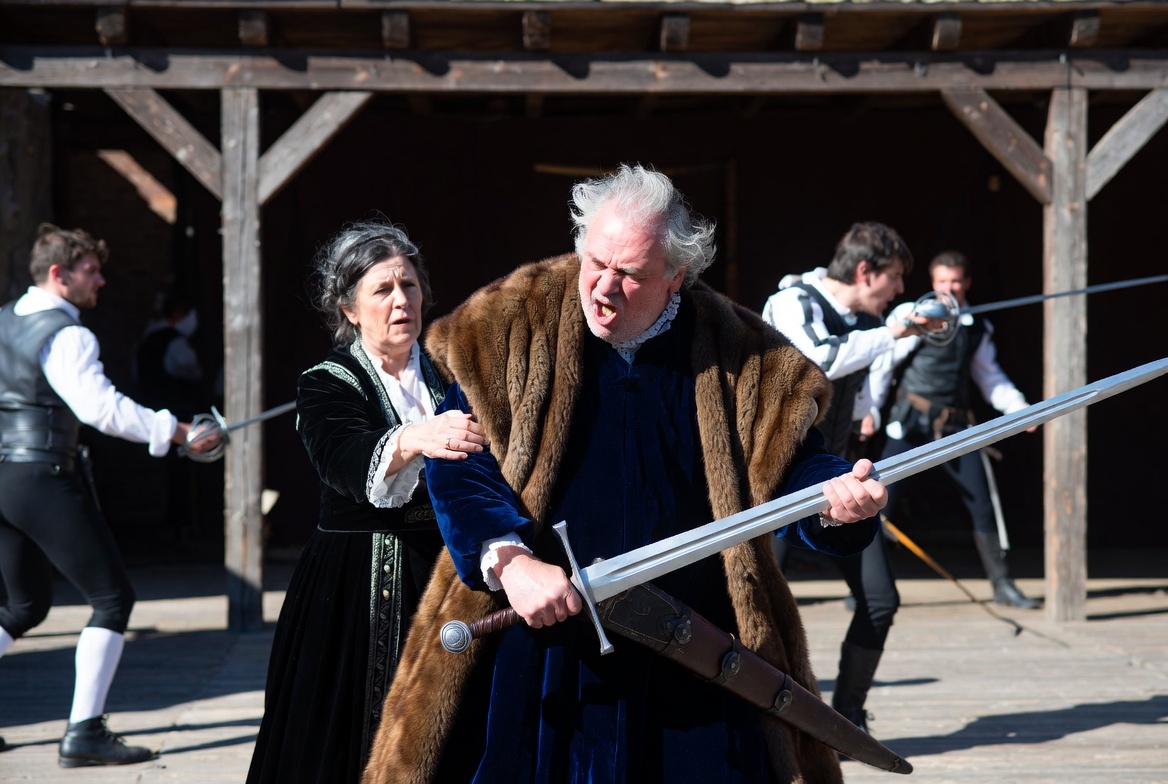 "An elderly noble character reaching for an English longsword during a stage fight, symbolizing historical generational conflict."
