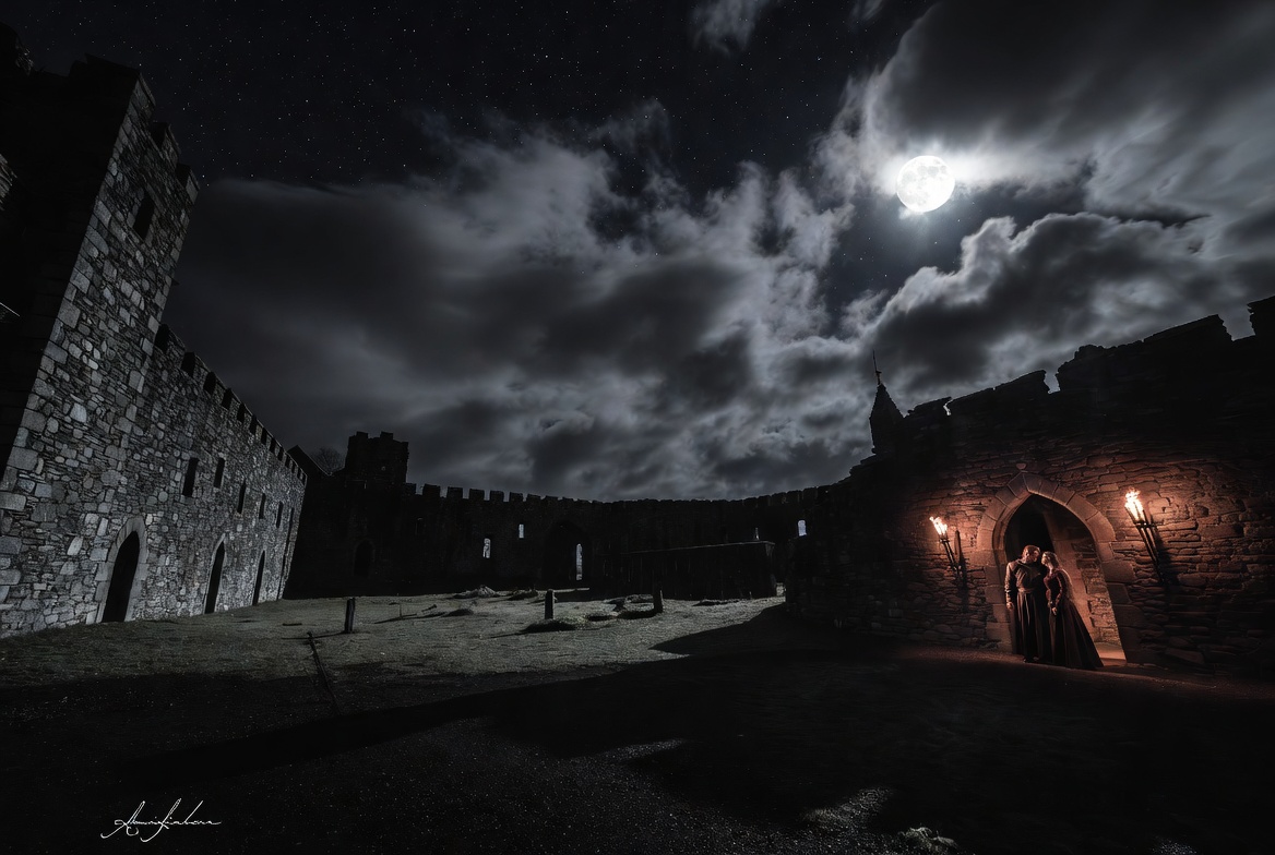 Macbeth and Lady Macbeth whispering conspiratorially in the dark courtyard of Inverness castle at night before Duncan's murder.