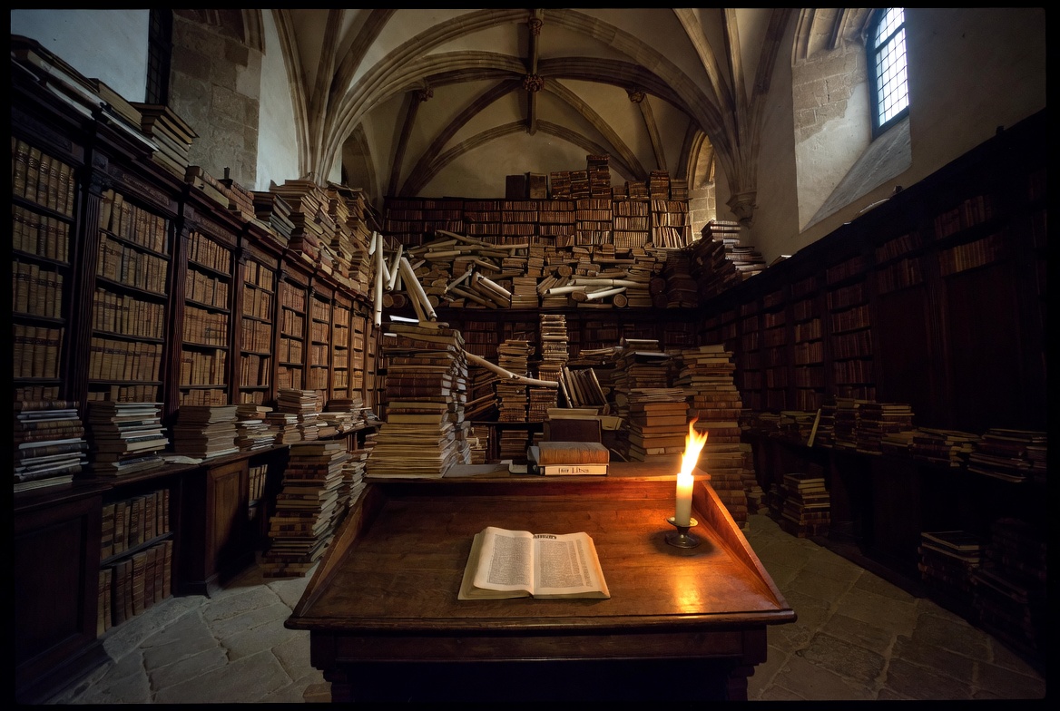 A symbolic photograph showing a small, thin manuscript labeled 180 LINES on a desk next to a massive, chaotic bookshelf in a dark medieval library.